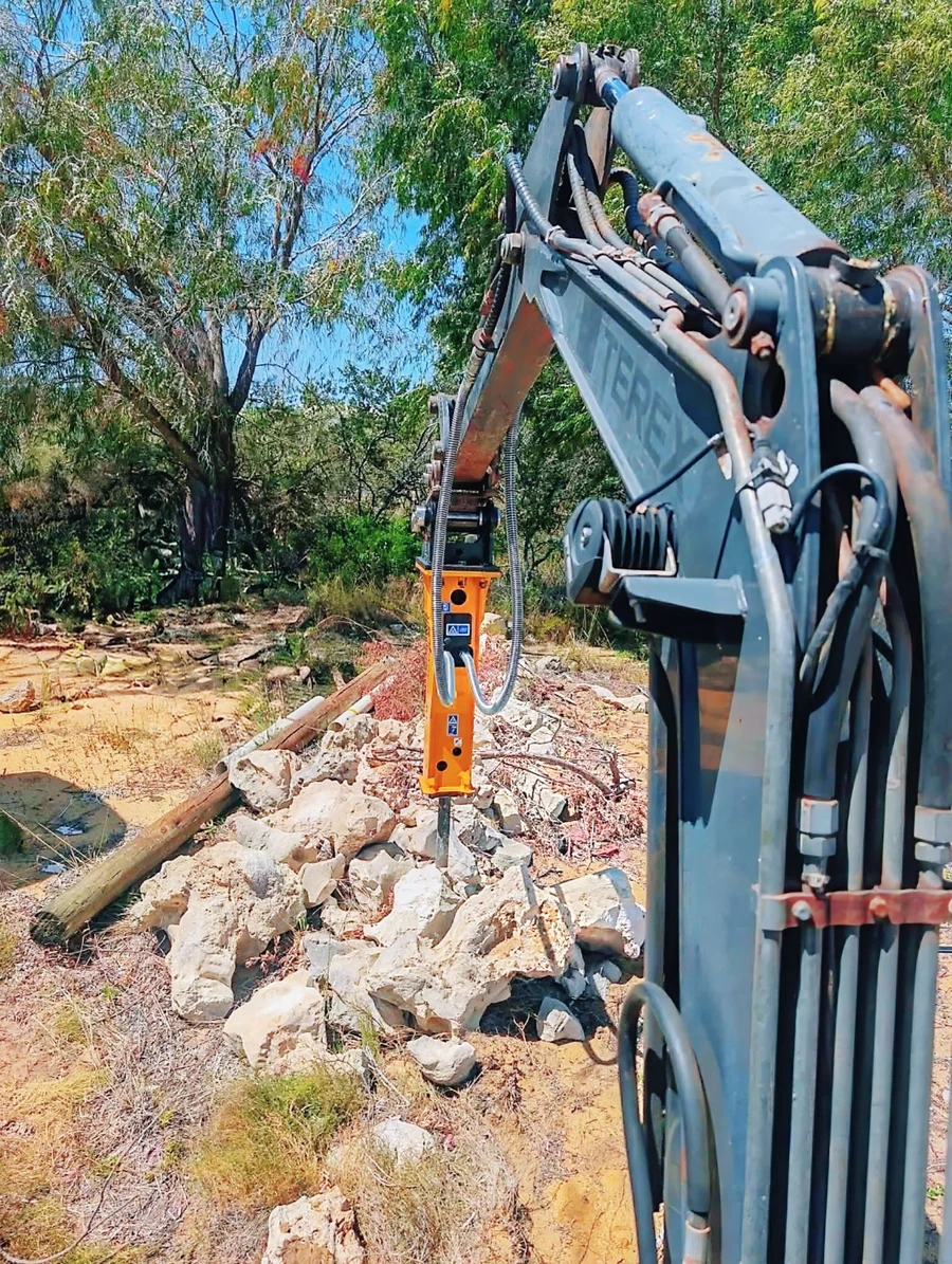 Mini excavator with a hydraulic rock breaker beside broken rock